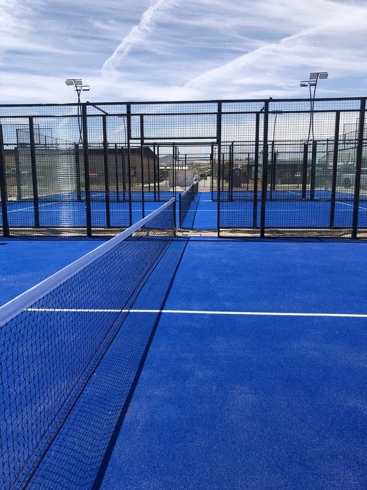 Padel net and blue playing surfaces with black mesh enclosures and court entrances.